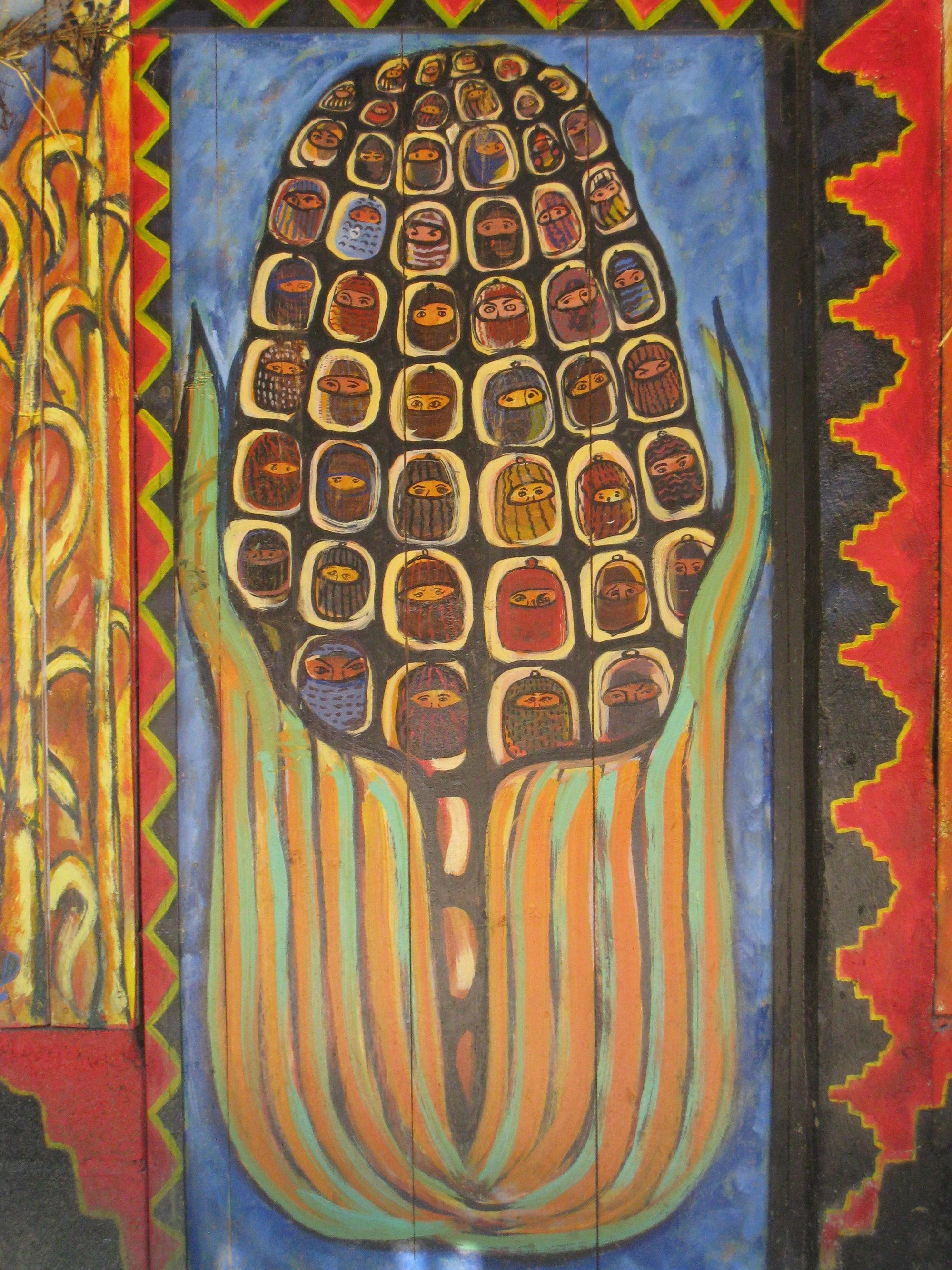 Close up of a painted mural of a large maize cob with faces painted on the kernels.