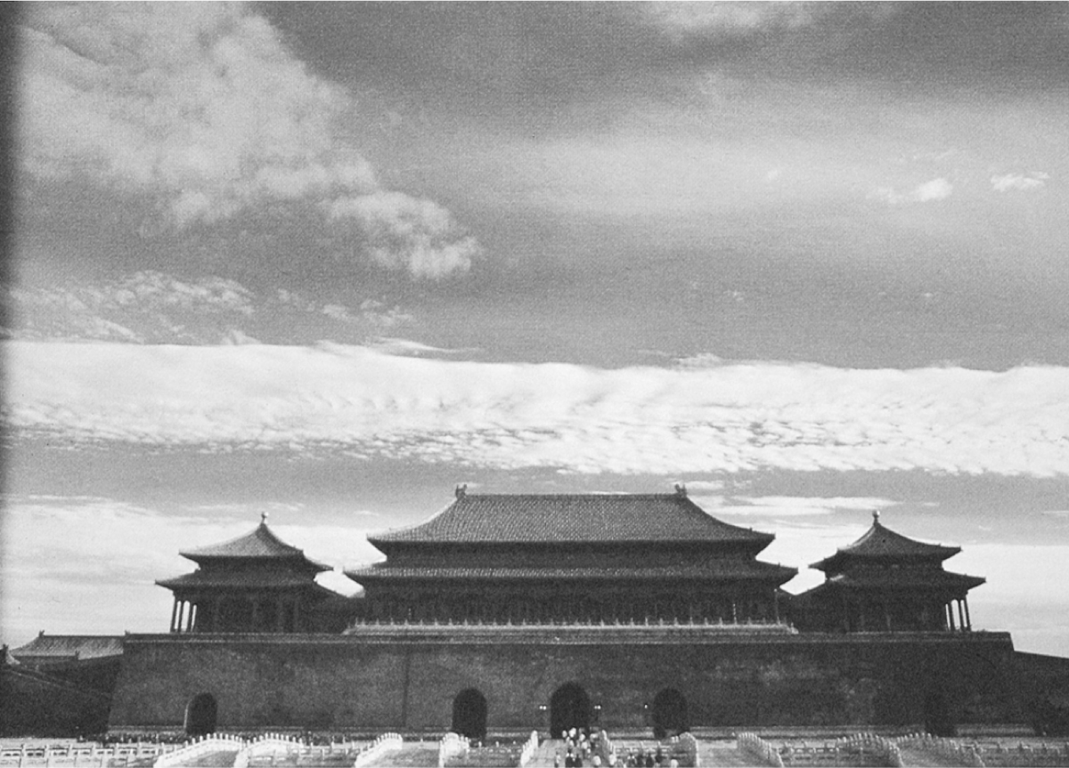 A photograph of an immense complex of buildings behind a tall, fortress-like wall. The broad, central building is flanked by two smaller buildings, one on each side. Each building appears to be 2-3 stories tall with tiered roofs.