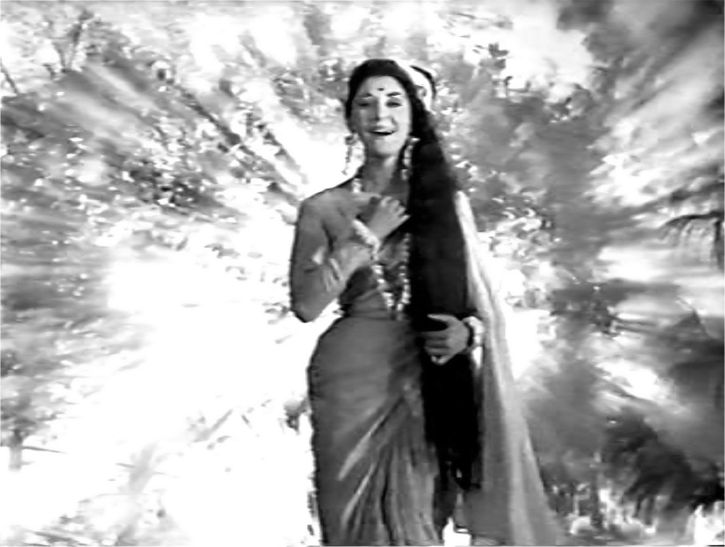 An exterior scene of a woman dressed in a sari with a forehead bindi, long hair, and a garland of flowers around her neck. She stands as a statuesque figure facing the camera, with radiating light emanating from the forest behind her.