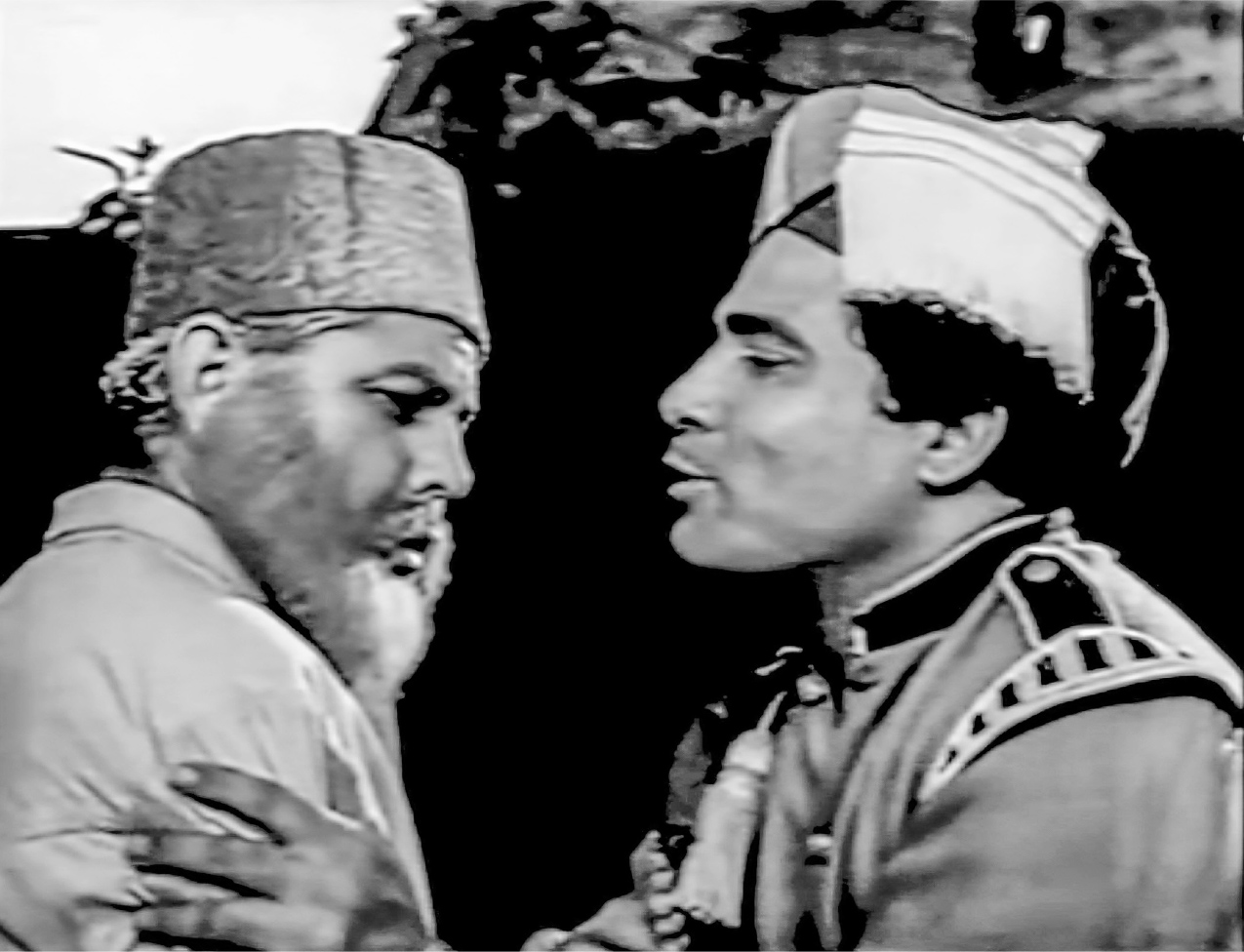 A close-up shot of an old man wearing a cap on the left and a man dressed in a pipe band costume and turban on the right, shown facing each other in profile and embracing.