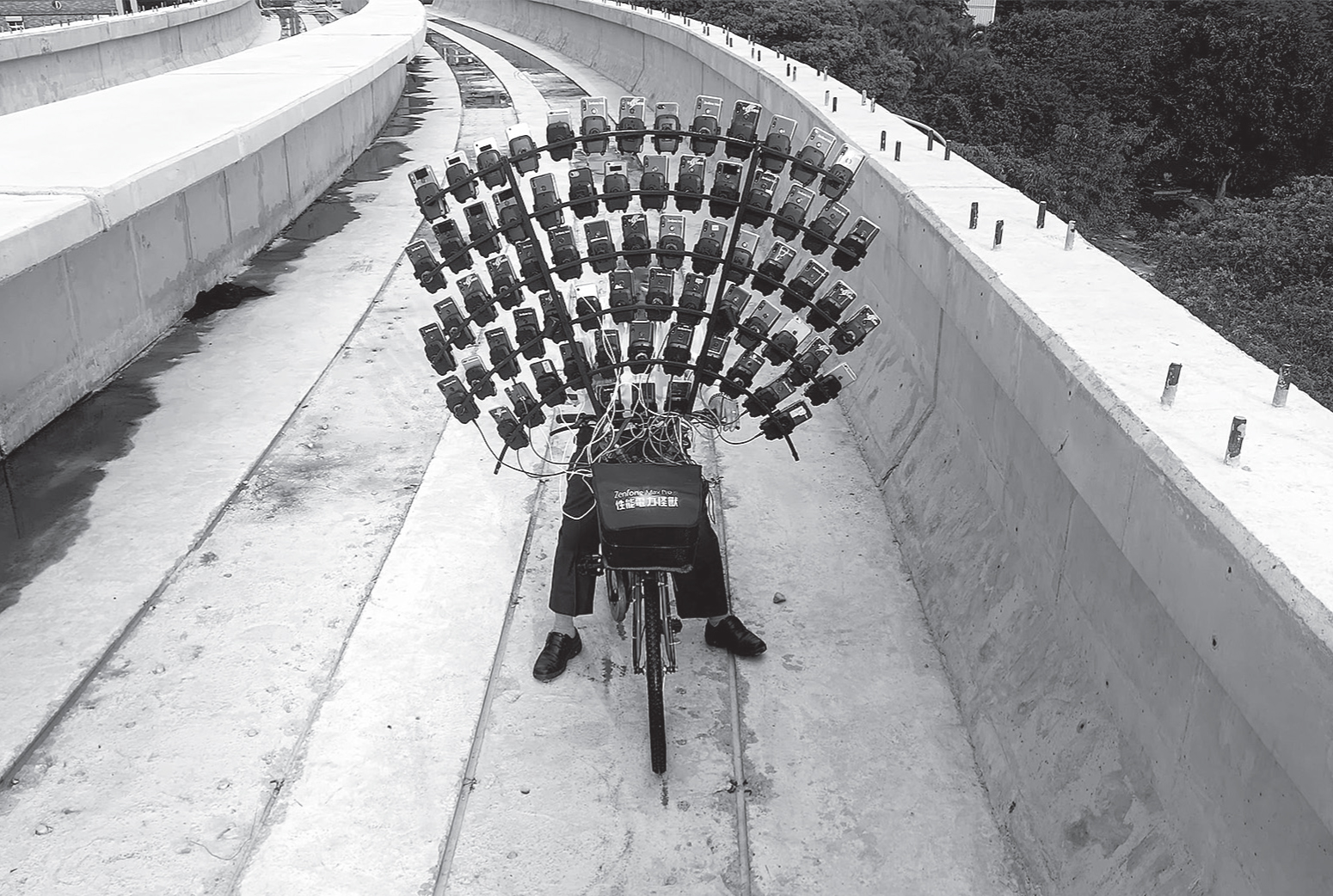 Frontside view of an older person straddling a bicycle looking at a fan-shaped arrangement of cell phones attached to the bike