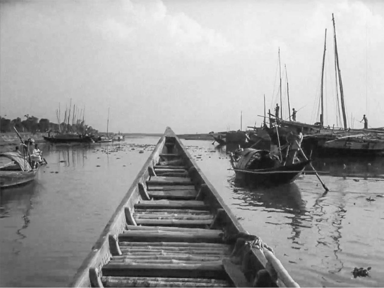 A shot of a boat’s triangular prow on open water, as seen from inside the boat, fills the center of the frame, with several other fishing boats moored on either side.