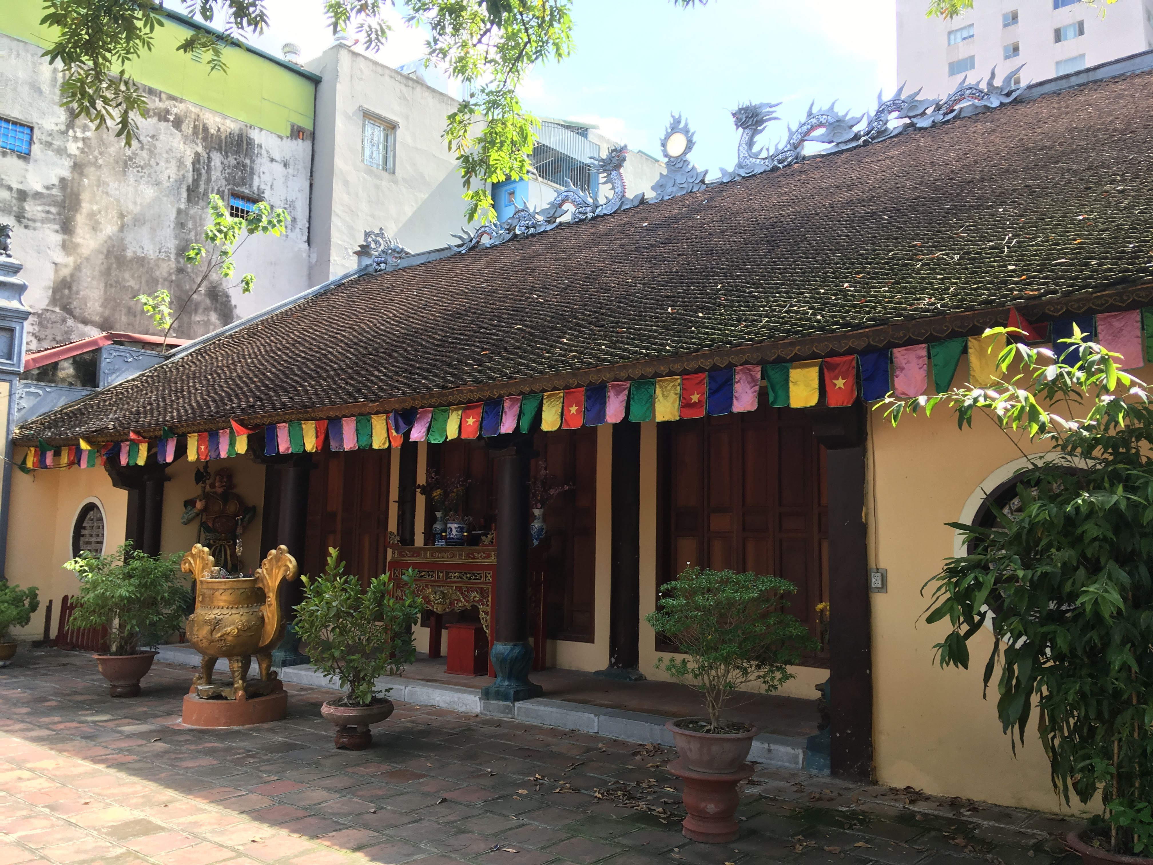 A low building with a small courtyard in front, a string of bright-colored flags on the roofline, and sculpted dragons on the roof’s peak.