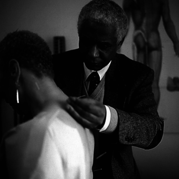 A person in a suit examining a person's back

Description automatically generated