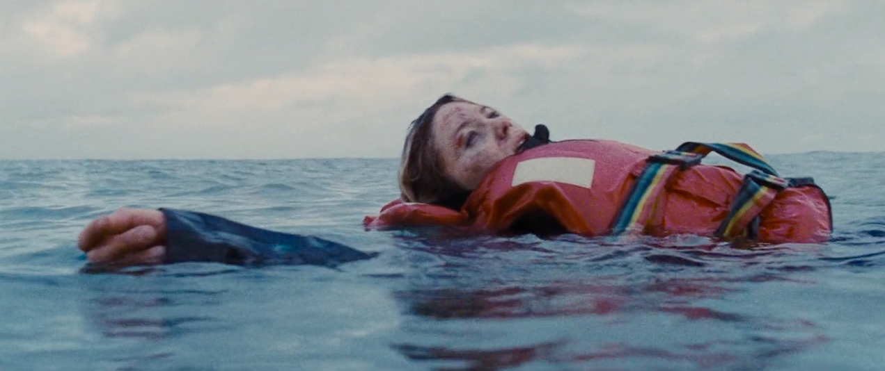 A close-up view of an exhausted woman wearing a life preserver floating on the surface of the sea as she looks up at the sky.