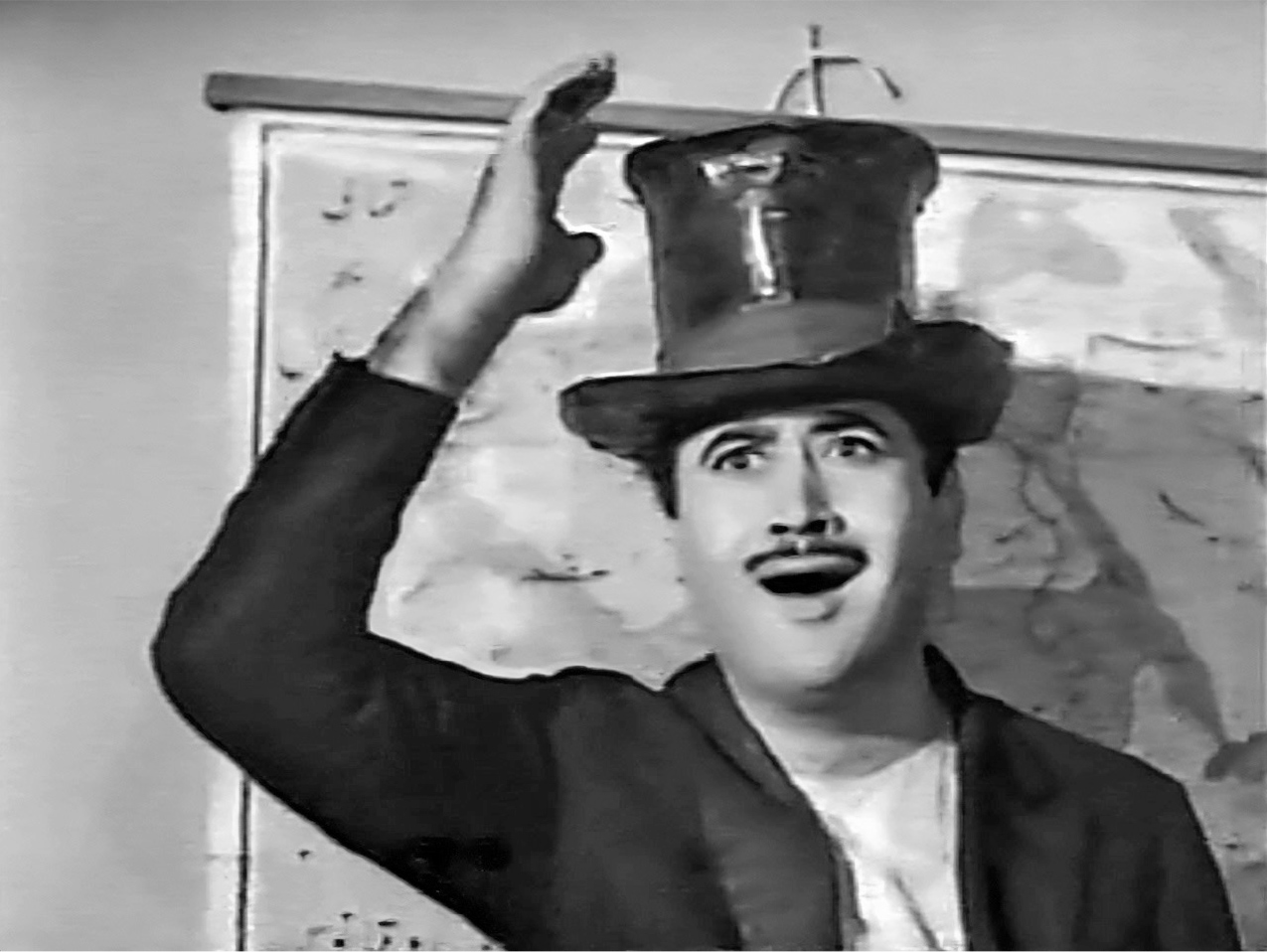 A medium close-up shot of a gesticulating man dressed in a coat and top hat in front of a large wall map.