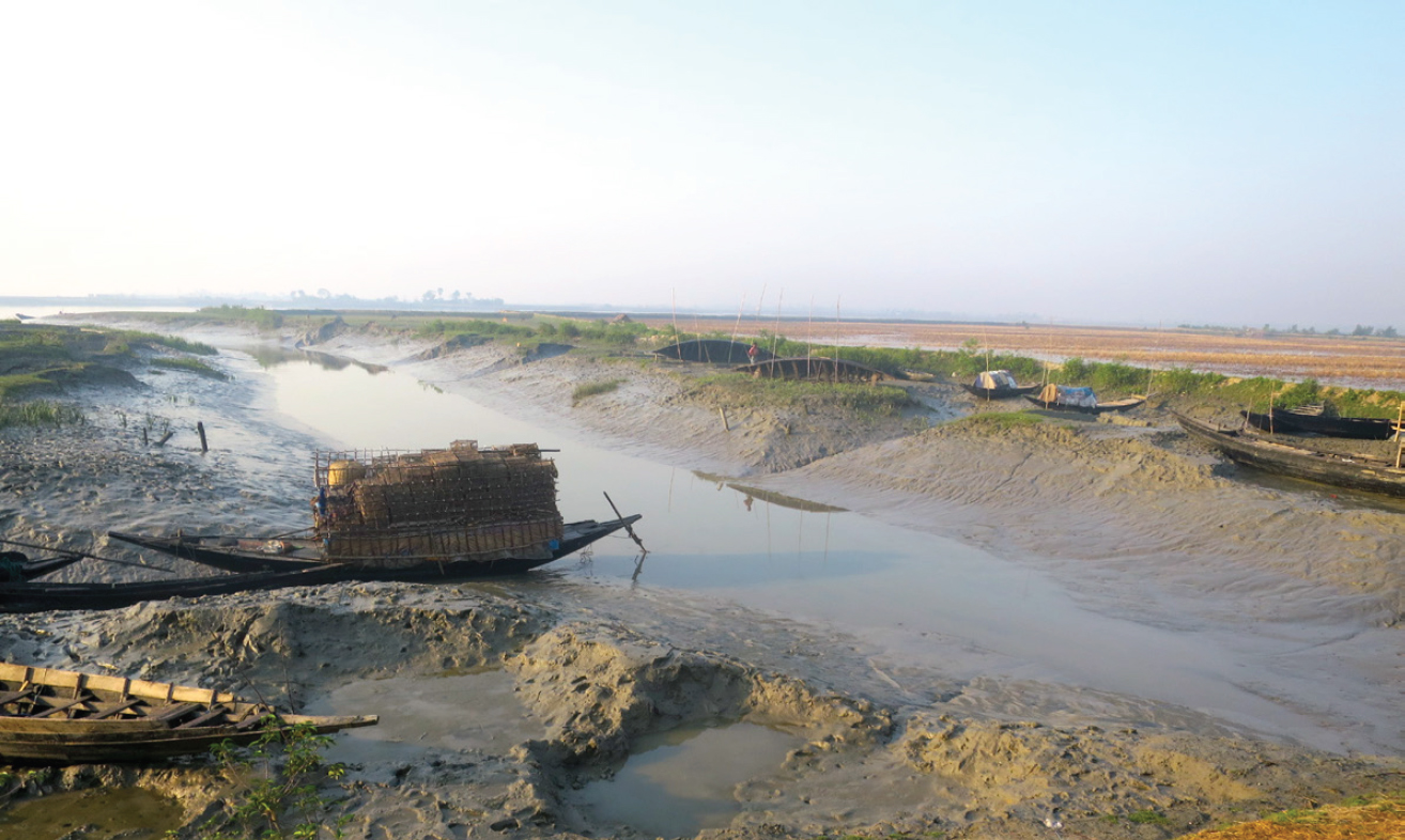A photograph of a stretch of still water flanked by sandy banks with small canoes pulled up on the shores.