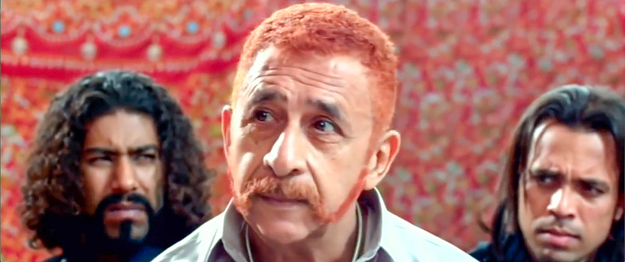A close-up of a man’s face, with the faces of two rough-looking men behind him on either side.