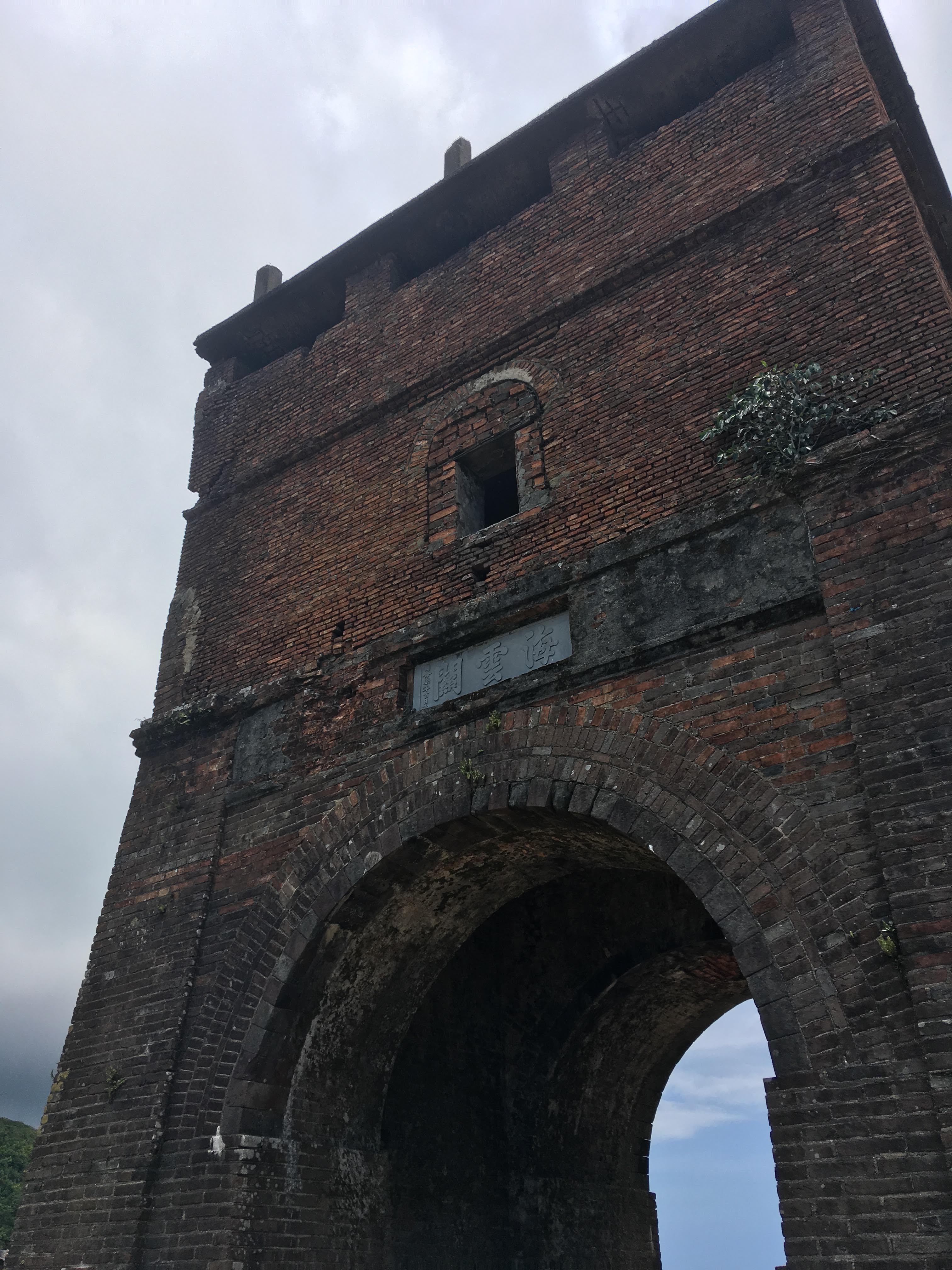 A tall, freestanding structure made of brick, with an open archway in the lower half and a small window in the story above.