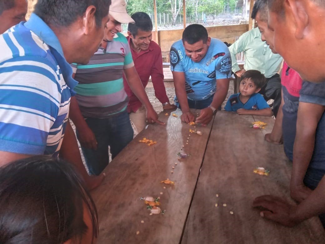 Men are crowded around a table with a row of kernels down the middle.