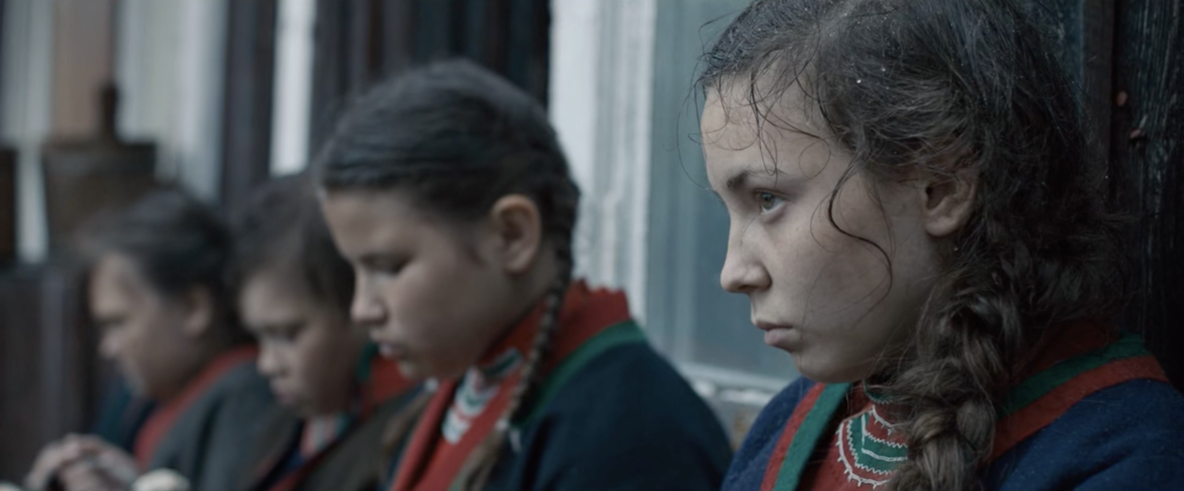 “A line of four girls in profile. The focus is on the first girl and the other three, with gazes downward, are blurred.”