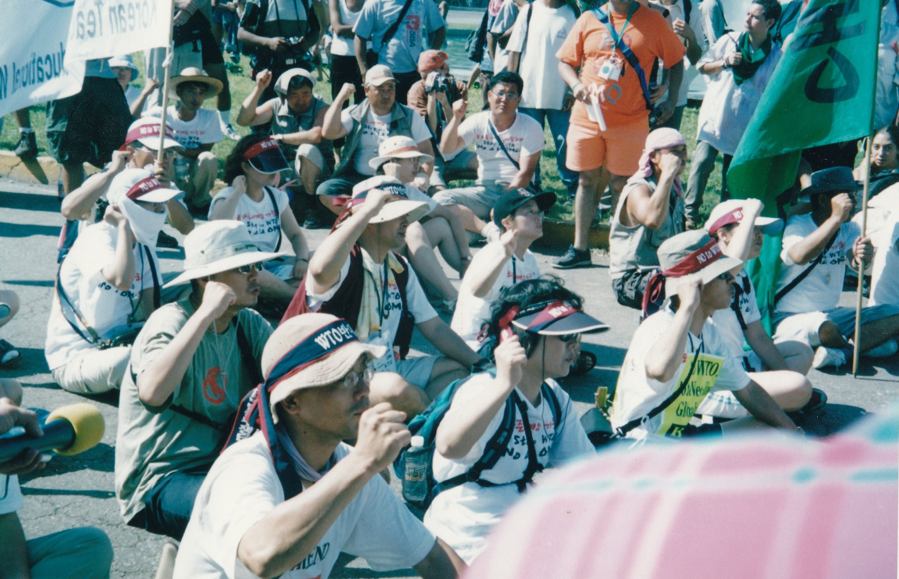 A group of people facing the same direction with their fists raised sit on the ground.