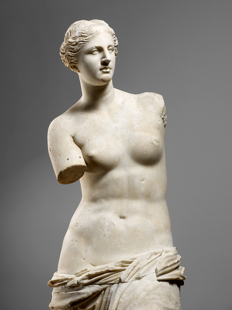 In this image, the famous Venus de Milo sculpture created by the artist 'Alexandros of Antioch' can be clearly seen against the solid grey background, allowing the white, Parian marble to stand out. The famous sculpture is a representation of the goddess of love, Aphrodite during the Hellenistic time. You can tell that the sculpture was made between 130-150 B.C. due to Aphrodite's absence of both arms when it was rediscovered. The top portion of Aphrodite is bare with only a draped garment that seems to slip off her hips. Her gaze is serene and neutral with her hair neatly pulled into the back just above hovering above her ears.