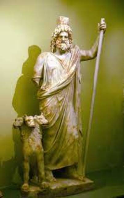 Statue of Hades and Cerberus against a green backround. He is represented holding up a stick,missing his other arm.